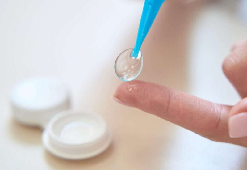 Close up picture of female hands is holding contact lenses above the table