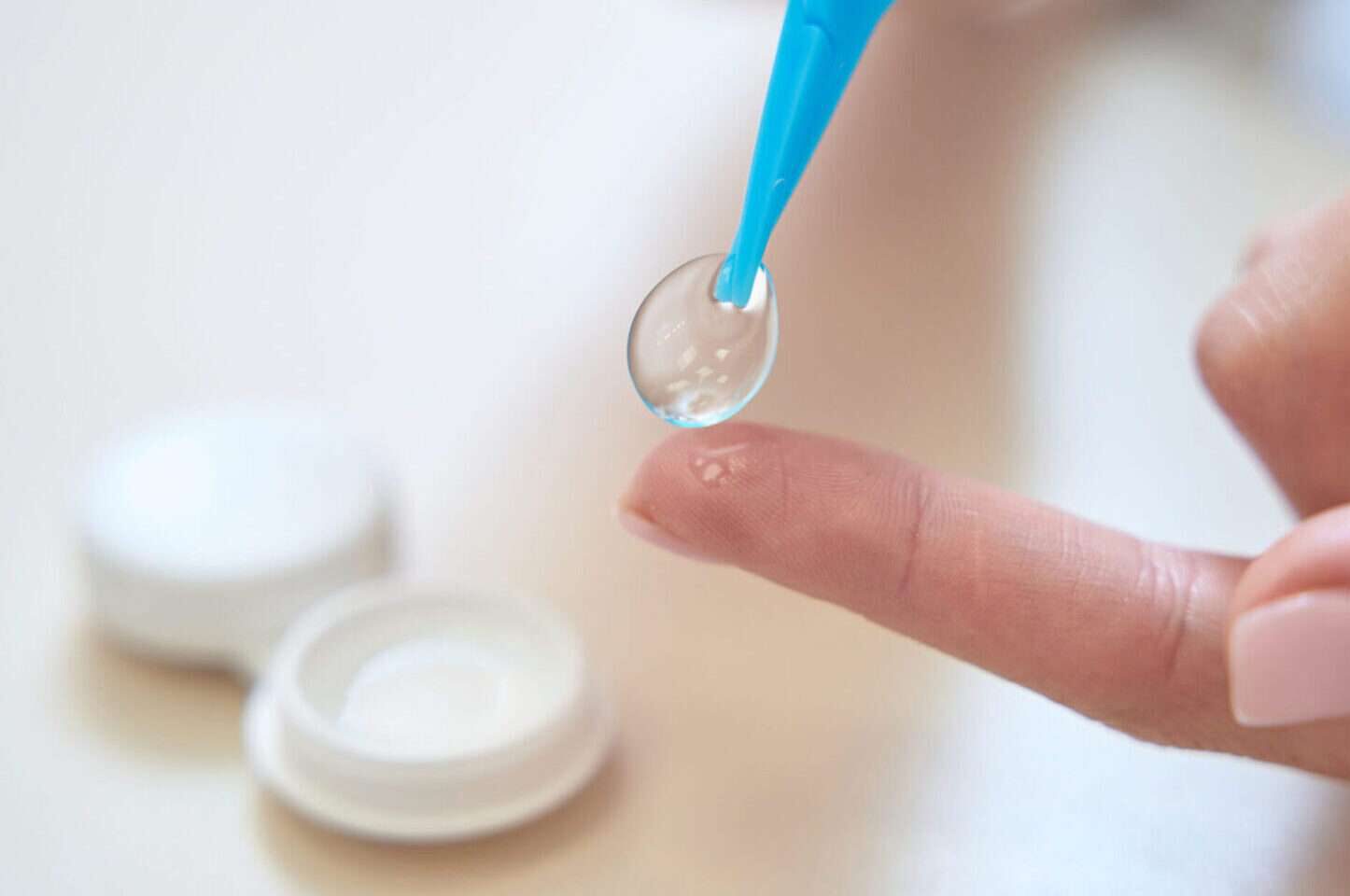 Close up picture of female hands is holding contact lenses above the table